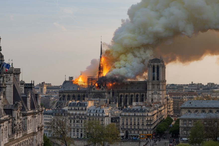 On voit la cathédrale Notre-Dame de Paris au centre de l’image et sur sa longueur. À droite la grande tour carrée, intacte. À gauche le clocher pointu en flammes avec le toit à sa gauche en flammes aussi. Au-dessus la fumée partant en diagonal vers la droite de l’image sous l’effet du vent. Cette photo vient de rtl.fr